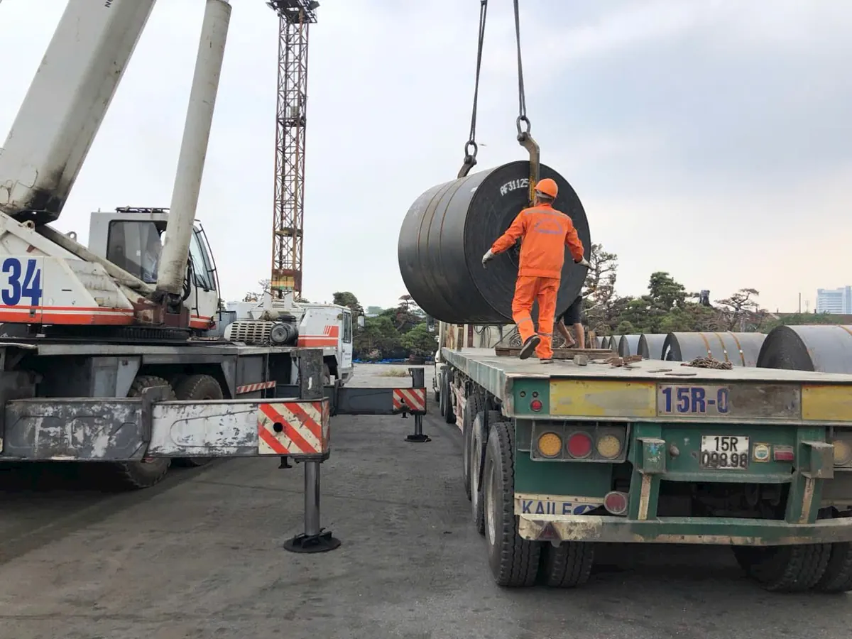 Công nhân hướng dẫn cẩu thép cuộn lên xe rơ moóc vận chuyển